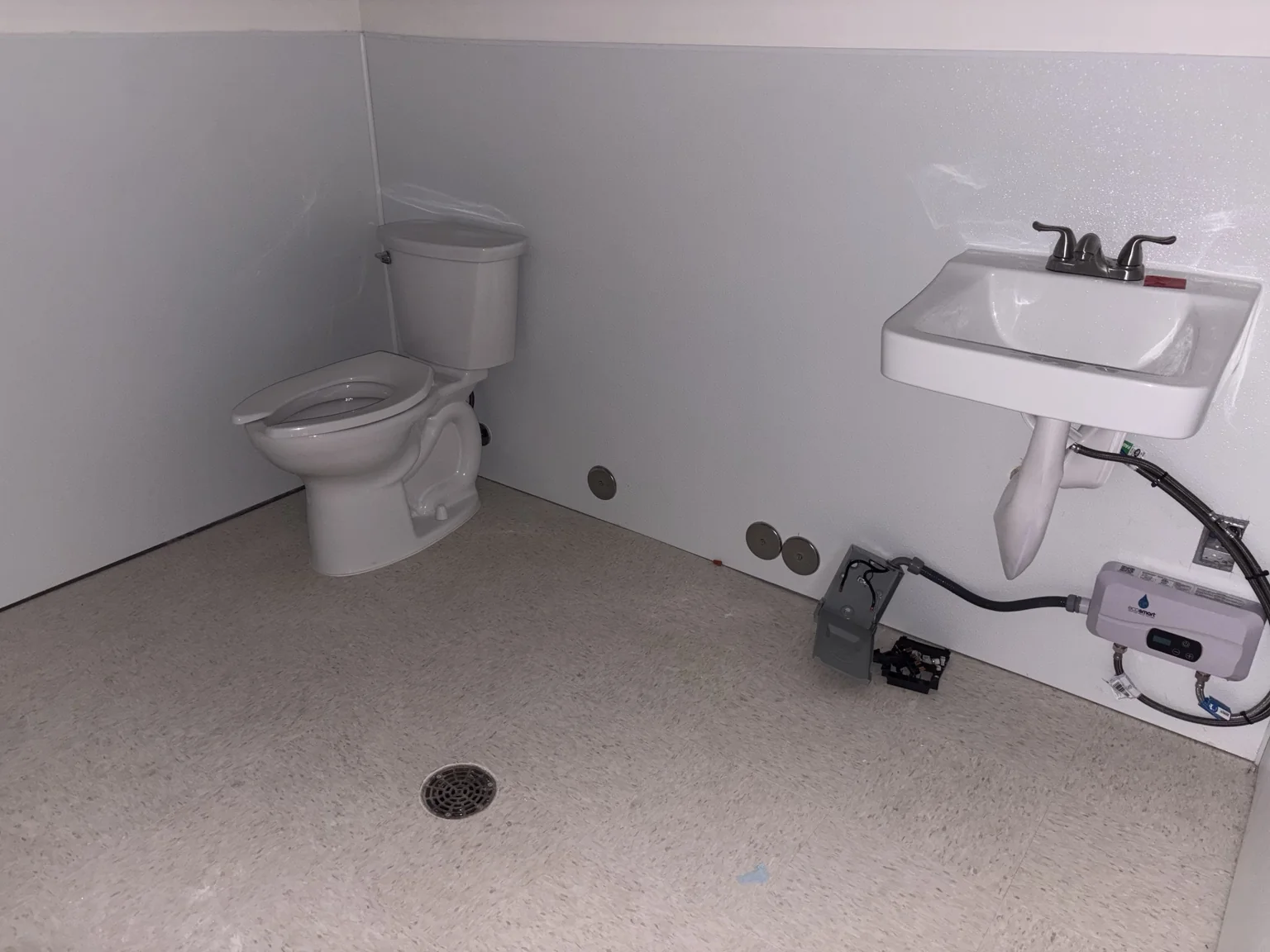 Finished restroom with toilet, wall-mounted lavatory, faucet, and floor drain