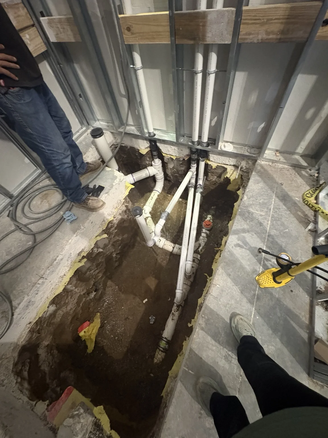 Open restroom slab showing PVC drain piping and branches before restoration